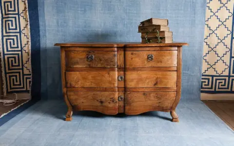 Cómoda de madera antigua, lista para pintar. Unos libros apilados descansan sobre ella.