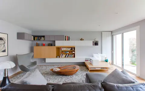 Salón moderno con estanterías empotradas y una **color crema pared**. Sofá de cuero, sillón gris y mesa de centro ovalada.