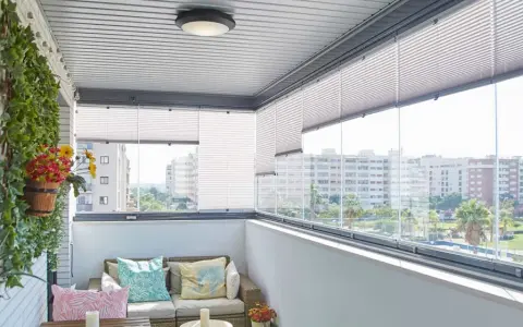 Ideas para tapar balcón: un espacio acogedor con sofá, plantas y vistas urbanas.