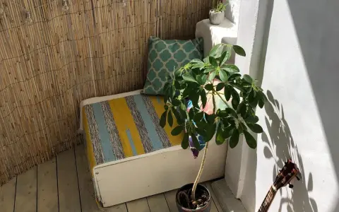 Un rincón acogedor para decorar balcon. Un banco con cojines, planta y luces crea un ambiente relajado.