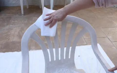 Mano limpia silla de plástico con paño, preparándola para pintura para plástico.