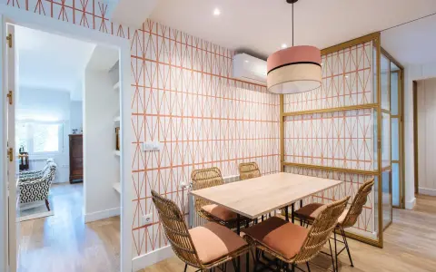 Comedor con pared empapelada con un diseño geométrico en naranja. Mesa de madera con sillas de ratán y cojines terracota.