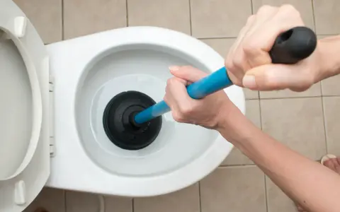 Manos usando un desatascador para como desatascar un water.