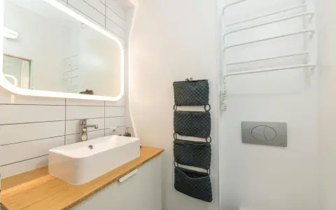 Moderno baño pequeño con lavabo sobre encimera de madera, espejo iluminado y organizadores de pared. ¡Una reforma de baño pequeño funcional y estilosa!