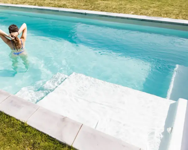 Mujer en bikini azul disfruta de una piscina cristalina, reflejo de un buen mantenimiento de piscinas.