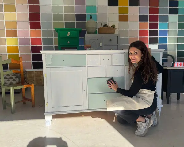 Mujer sonríe mientras trabaja en un mueble, demostrando cómo pintar muebles de madera sin lijar.