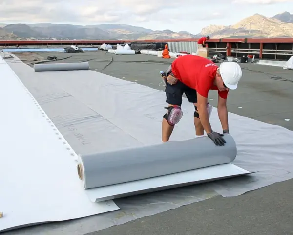 Trabajadores instalan un rollo de material para el aislante térmico exterior en una obra.