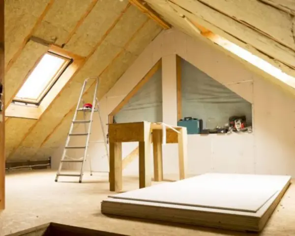 Techo interior en proceso de aislamiento. Se ve el aislante térmico para techos interiores, escalera, materiales de construcción y una ventana de tejado.