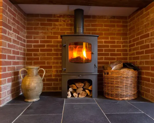 Estufa de leña con fuego encendido, chimenea de ladrillo, leña en cesta y jarrón. Guía para como instalar una estufa de leña con salida horizontal.