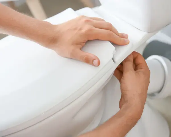 Man's hands carefully fitting the toilet seat, part of the process to como instalar un inodoro al suelo.