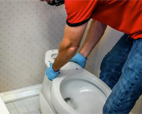 Hombre con guantes azules desmonta asiento de inodoro. Aprende como quitar un bidet para renovar tu baño.