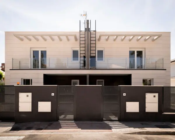 Moderna fachada ventilada de piedra clara con balcones de cristal y rejas oscuras.