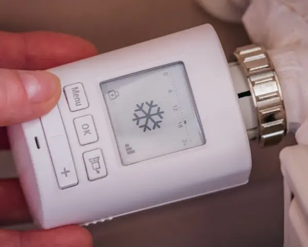 Termostato digital para sistemas de calefacción, con pantalla que muestra un copo de nieve y botones para ajustar la temperatura.