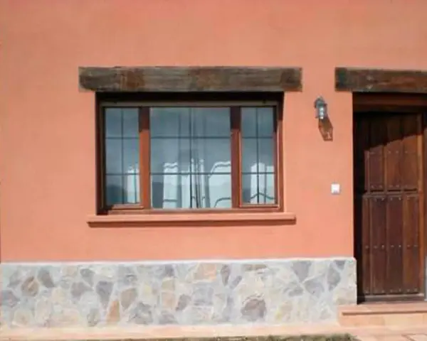 Fachada con zócalo de piedra irregular, ventana de madera y puerta rústica. Muestra distintos tipos de zócalos para paredes exteriores.