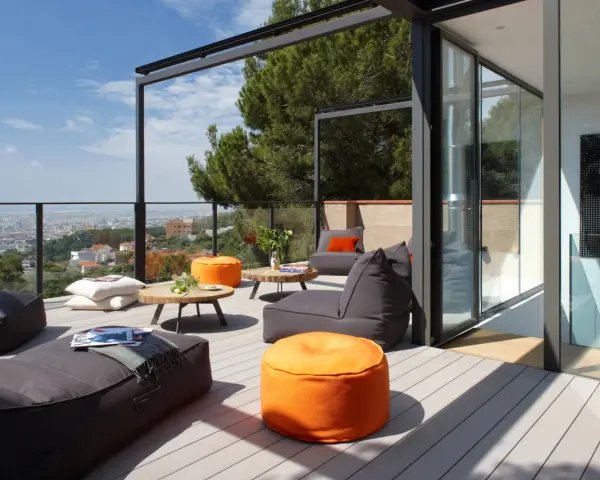 Cómoda terraza ático con sillones y pufs naranjas, vistas a la ciudad y un gran pino.