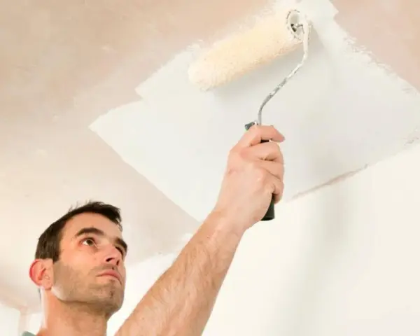 Hombre pintando el techo con rodillo. La pregunta de si que se pinta primero el techo o las paredes es clave para un buen acabado.