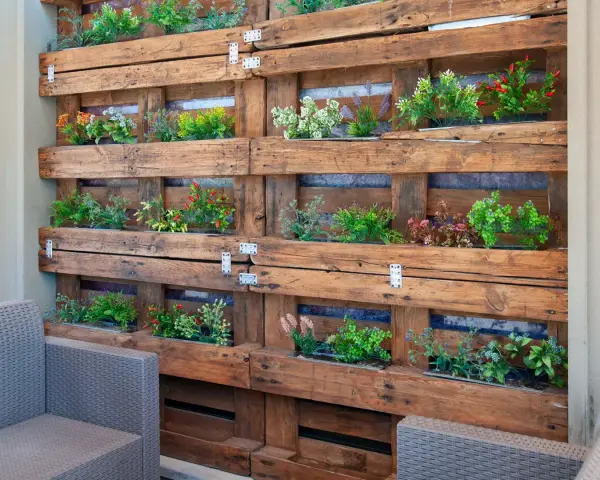 Jardineras con palets crean un jardín vertical lleno de plantas verdes y flores de colores, un oasis en el balcón.