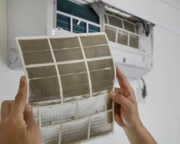 Manos sostienen un filtro de aire acondicionado sucio, mostrando cómo cambiarlo para un aire más limpio.