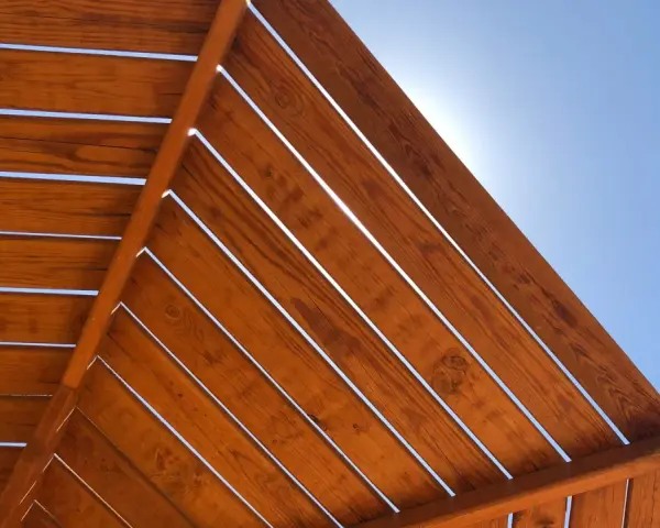 Estructura de madera con tratamiento para exterior, con lamas de madera barnizada bajo un cielo azul brillante.