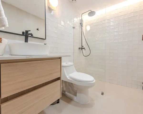 Baño moderno con lavabo sobre mueble de madera, inodoro y ducha con azulejos blancos. ¡Un proyecto de pintar azulejos baño que inspira!