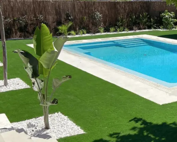 Jardín moderno con piscina y césped artificial. La colocación de césped artificial realza la belleza del espacio.