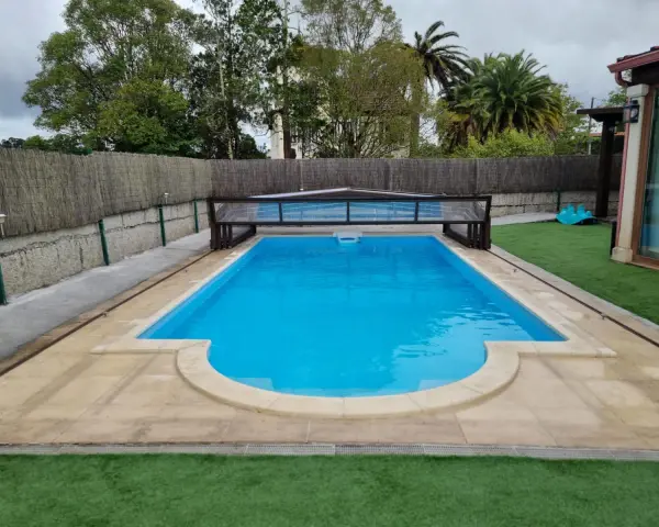 Piscina con cubierta retráctil, rodeada de césped artificial y un sistema para canalizar agua de lluvia.