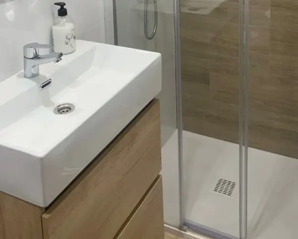 Lavabo moderno con mueble de madera y ducha acristalada. Un ejemplo de cuartos de baño modernos y funcionales.