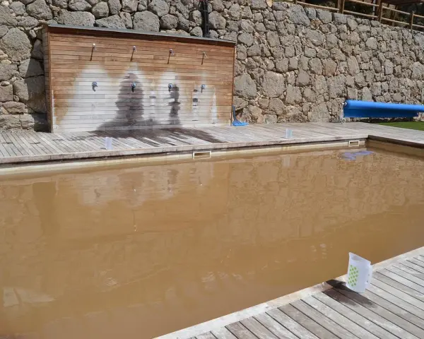 Una piscina de agua salada con un revestimiento de madera y duchas. El agua es de color marrón turbio.