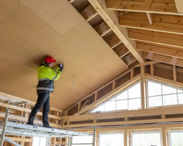 Trabajador en andamio instala paneles aislantes en el techo, parte de un proyecto para como aislar una casa ya construida.