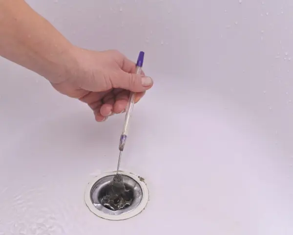 Mano usando un bolígrafo para quitar pelo y desatascar la ducha.