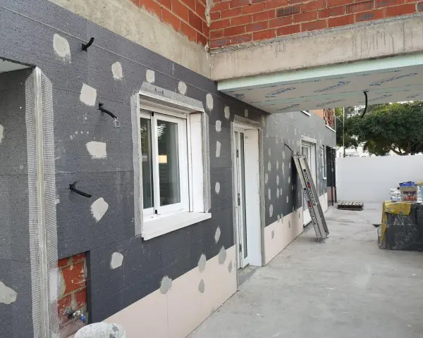 Fachada en construcción con aislamiento SATE, tuberías y ventanas.