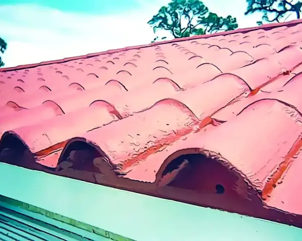 Tejas rojas de barro en un tejado, ideal para reparar tejado sin quitar tejas. Cielo azul y árboles al fondo.