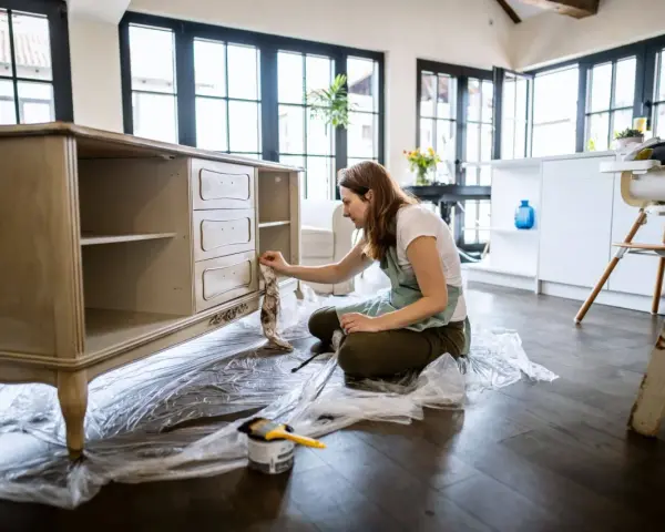 Mujer aplicando una capa de pintura a un mueble antiguo.