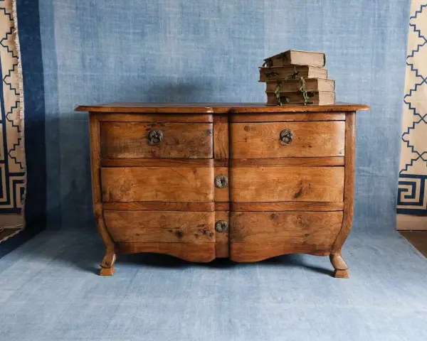 Cómoda de madera antigua, lista para pintar. Unos libros apilados descansan sobre ella.