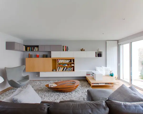 Salón moderno con estanterías empotradas y una **color crema pared**. Sofá de cuero, sillón gris y mesa de centro ovalada.