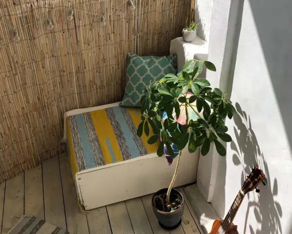 Un rincón acogedor para decorar balcon. Un banco con cojines, planta y luces crea un ambiente relajado.