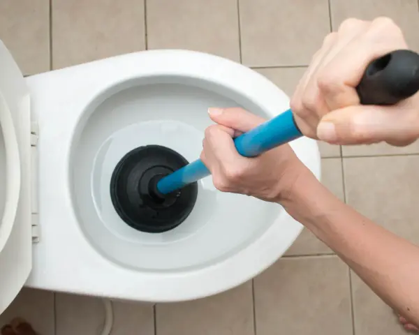 Manos usando un desatascador para como desatascar un water.