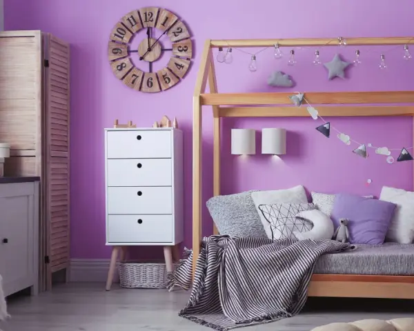 Adolescentes pintan habitación juvenil. Un espacio lleno de color lila, con cama de madera, cómoda blanca y decoración infantil.