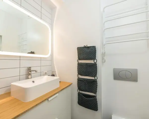 Moderno baño pequeño con lavabo sobre encimera de madera, espejo iluminado y organizadores de pared. ¡Una reforma de baño pequeño funcional y estilosa!