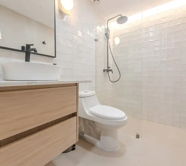 Baño moderno con lavabo sobre mueble de madera, inodoro y ducha con azulejos blancos. ¡Un proyecto de pintar azulejos baño que inspira!
