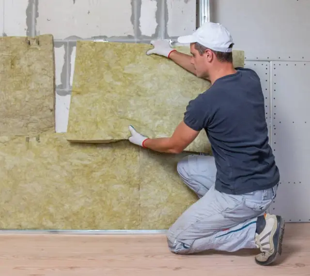 Un hombre instala aislamiento en una pared para combatir el frío en casa.