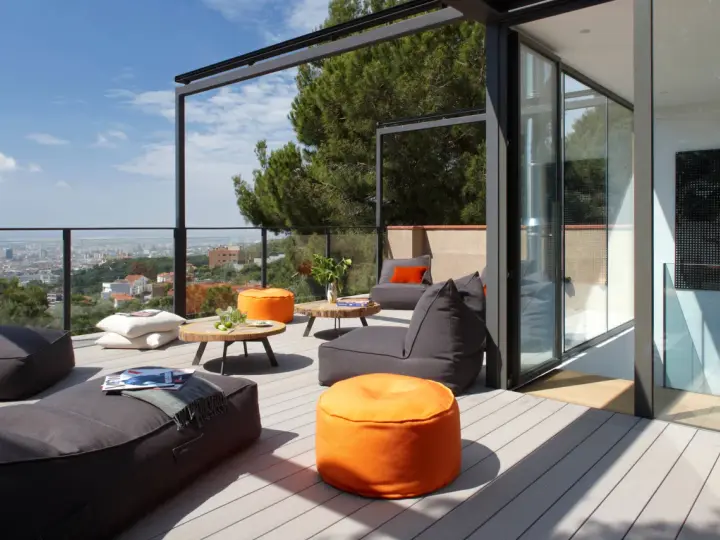 Cómoda terraza ático con sillones y pufs naranjas, vistas a la ciudad y un gran pino.