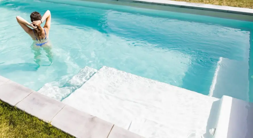 Mujer en bikini azul disfruta de una piscina cristalina, reflejo de un buen mantenimiento de piscinas.