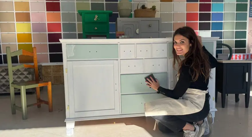 Mujer sonríe mientras trabaja en un mueble, demostrando cómo pintar muebles de madera sin lijar.