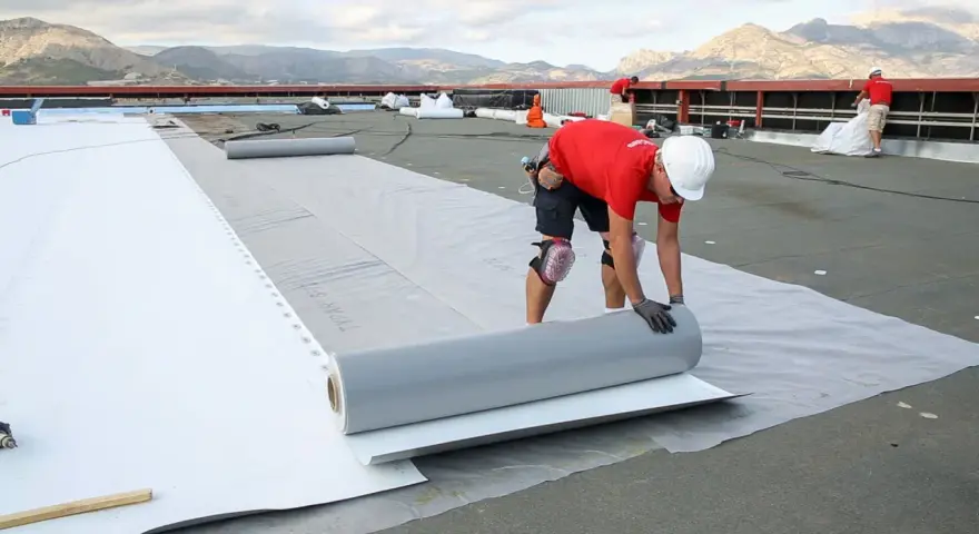Trabajadores instalan un rollo de material para el aislante térmico exterior en una obra.