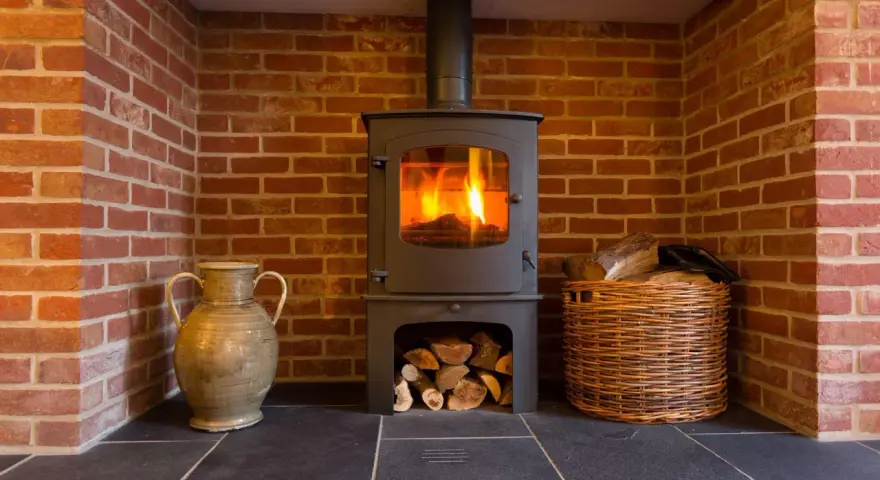 Estufa de leña con fuego encendido, chimenea de ladrillo, leña en cesta y jarrón. Guía para como instalar una estufa de leña con salida horizontal.