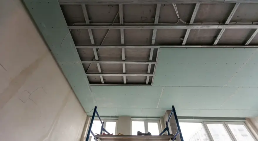 Instalación de falso techo de pladur para insonorizar habitación de ruidos de vecinos. Andamio y estructura metálica visibles.