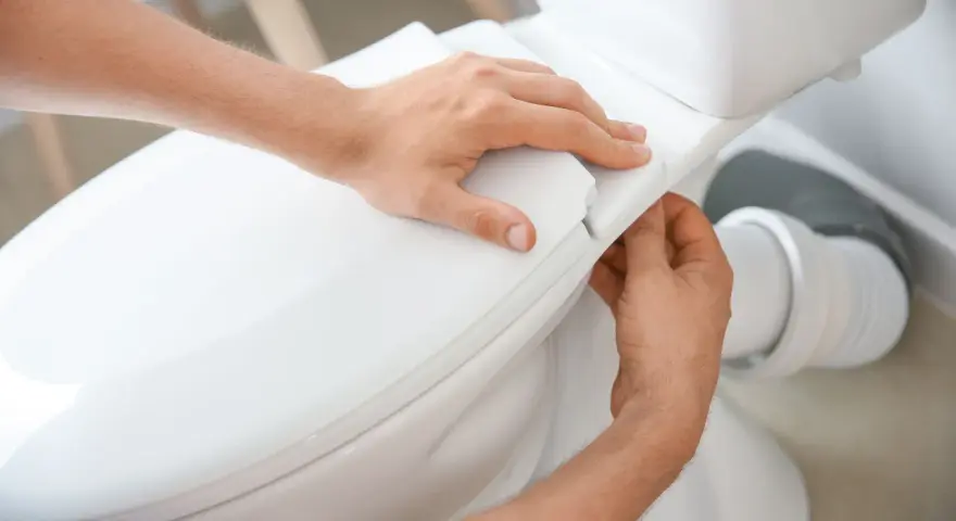 Man's hands carefully fitting the toilet seat, part of the process to como instalar un inodoro al suelo.