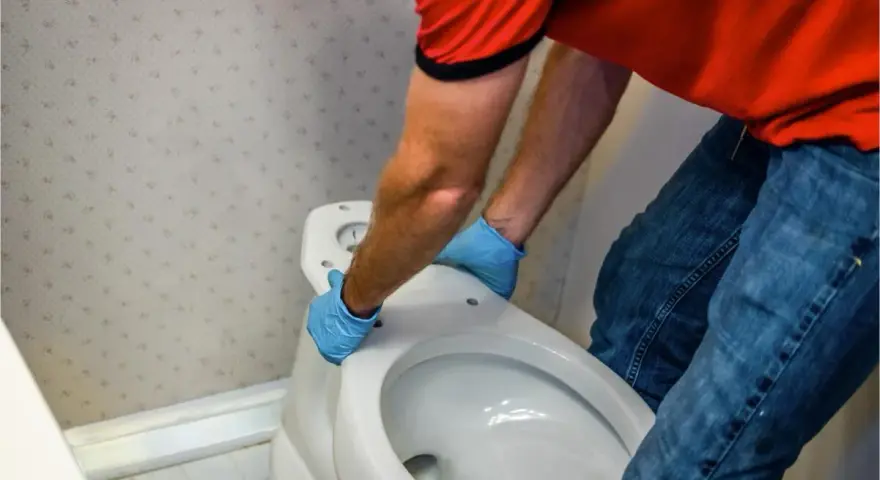 Hombre con guantes azules desmonta asiento de inodoro. Aprende como quitar un bidet para renovar tu baño.