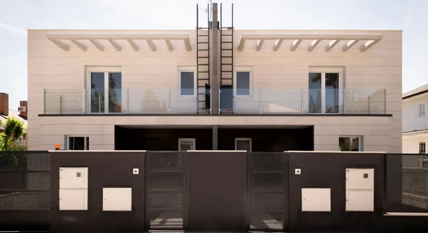 Moderna fachada ventilada de piedra clara con balcones de cristal y rejas oscuras.